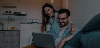 Imagem de um casal sorrindo, olhando para a tela de um notebook