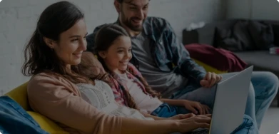 Imagem de uma família sentados ao sofás, mexendo em um notebook